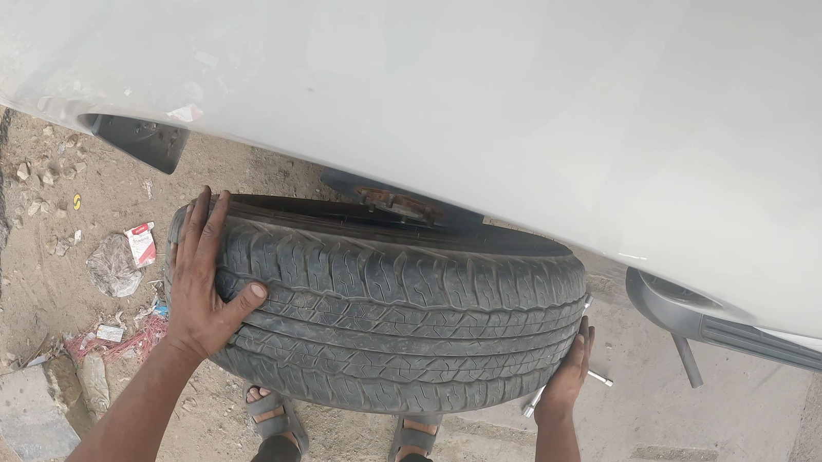 First-person view of hands carrying two tires beside a vehicle
