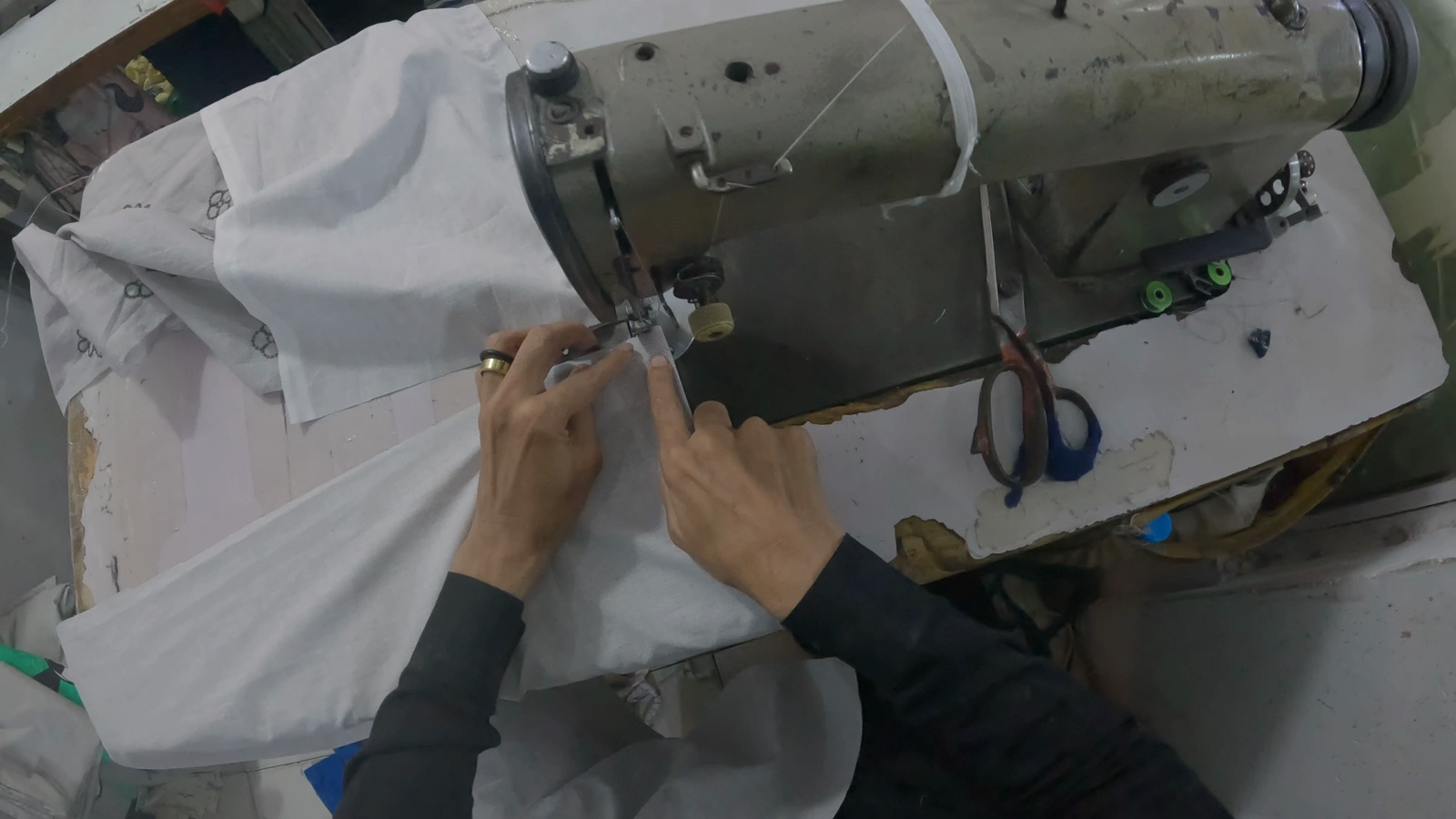Hands guiding fabric beneath a sewing machine needle